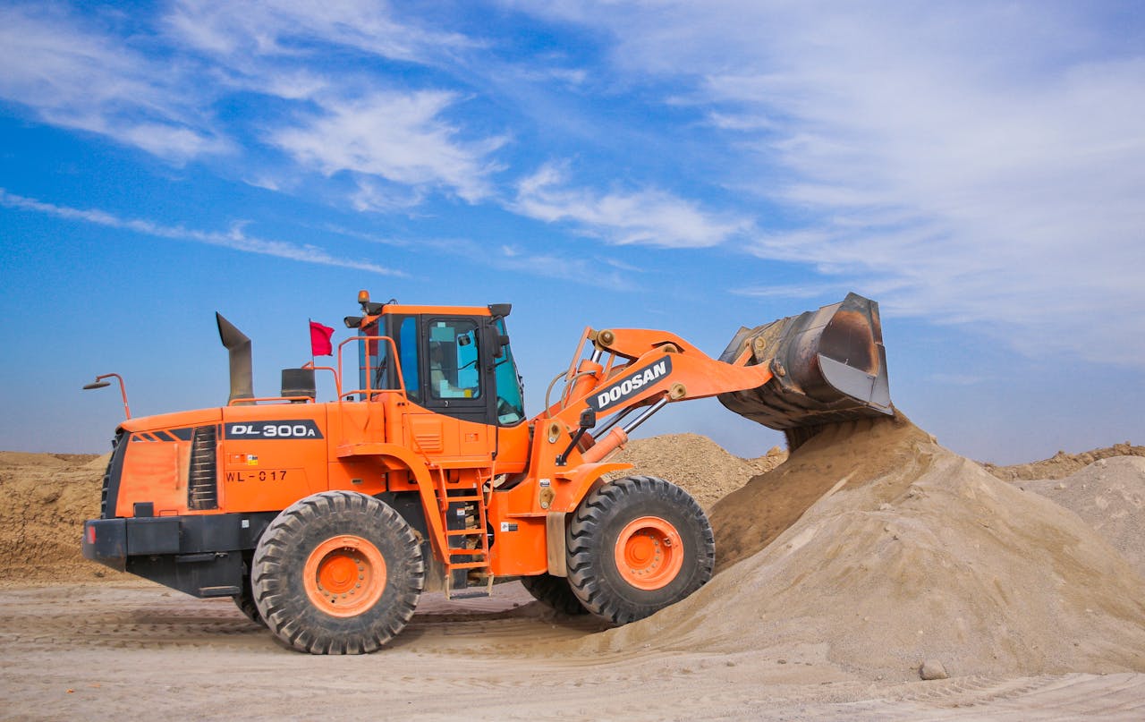 about-03 An orange bulldozer at work, moving sand under a clear blue sky on a construction site.