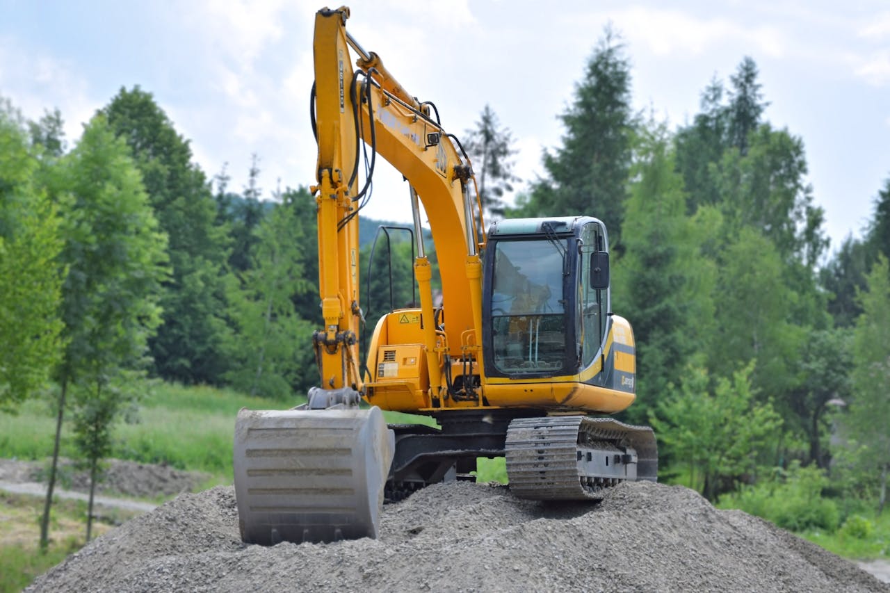 about-02 A yellow excavator on a pile of gravel in a lush, green forest setting in Poland.